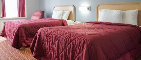 A hotel room with two beds, each with a wooden headboard and white pillows. There is a red chair and a bedside table with a phone.