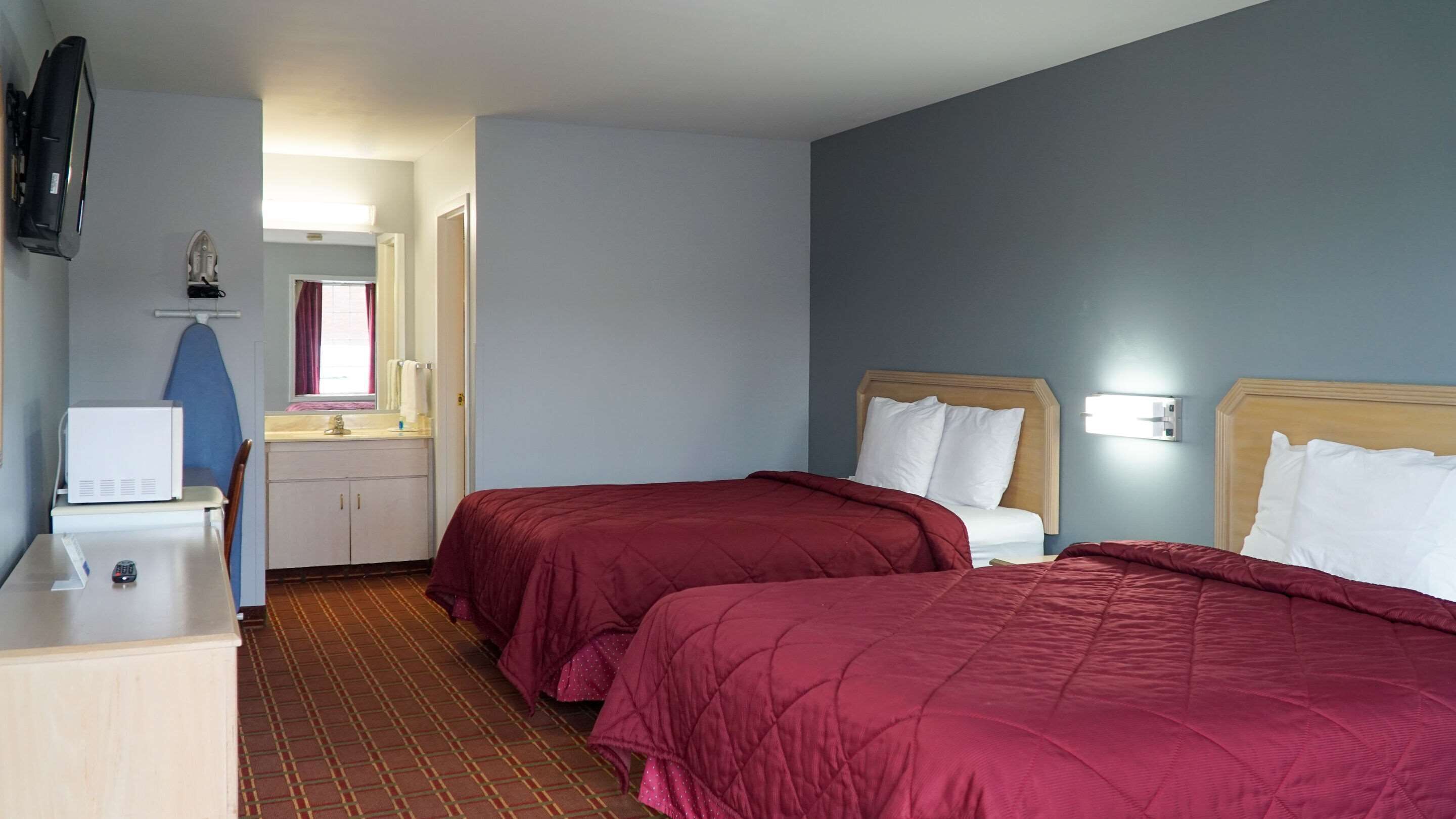 A hotel room with two beds, a desk with a computer, a mirror, and a window with curtains.