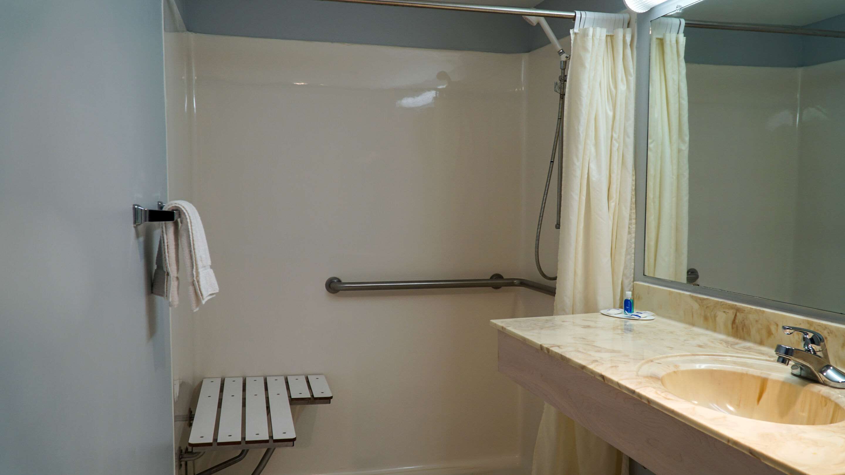 A bathroom with a shower, a towel rack, a hand dryer, a sink, and a mirror.