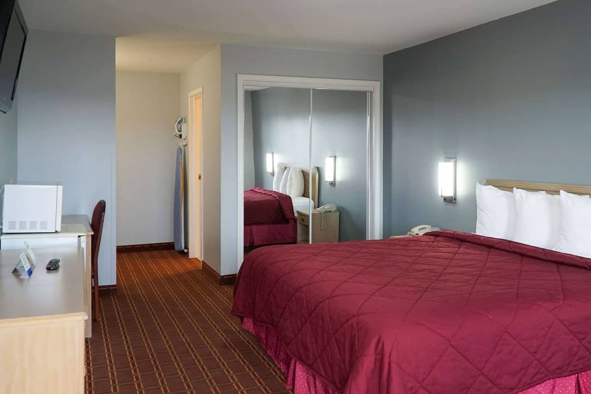 A hotel room with a bed, a desk, a chair, a microwave, and a telephone.