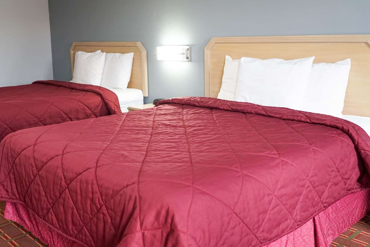Two queen-sized beds with red bedding, wooden headboards, and a light switch on the wall.