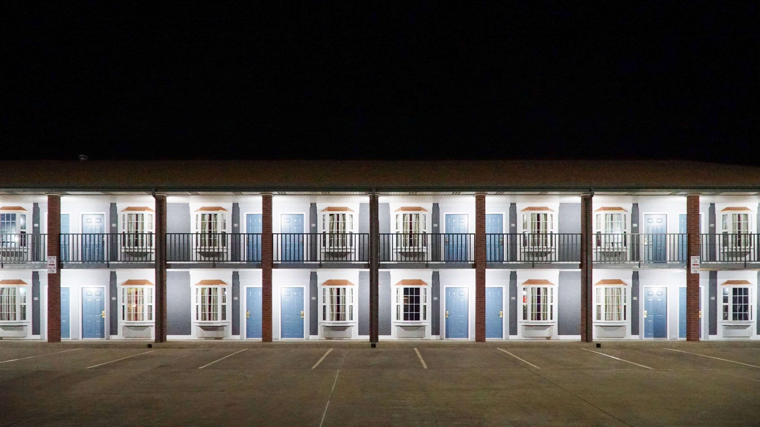 A two-story motel with a row of rooms, each with a balcony and a door.