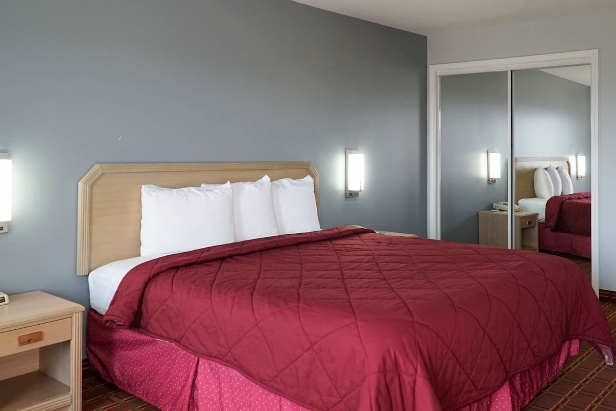 A hotel room with a bed, a nightstand, a mirror, and a wardrobe.