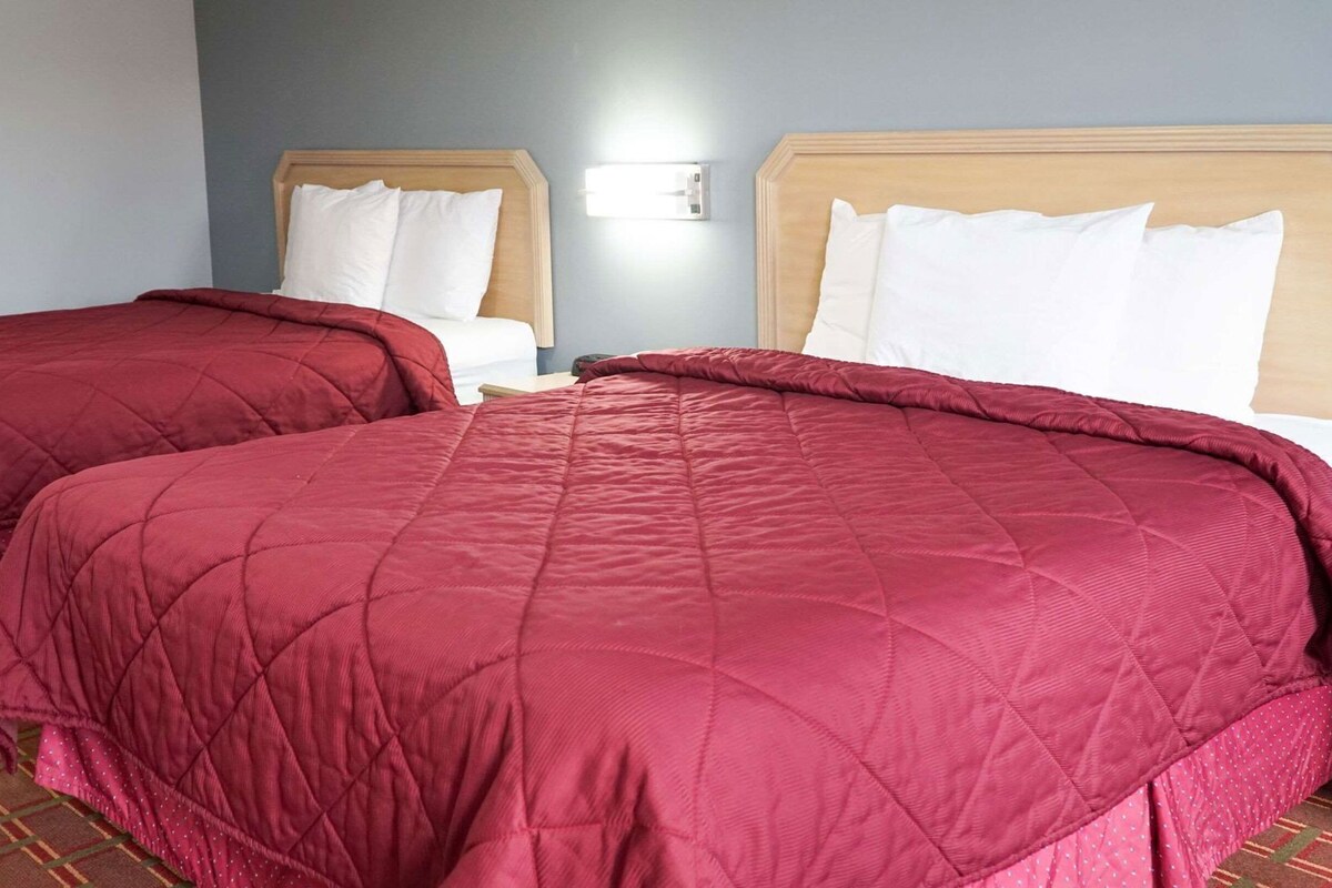 Dos camas con ropa de cama roja, un cabecero de madera y un interruptor de luz en la pared.