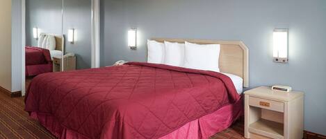 A hotel room with a large bed, a bedside table with a lamp, a mirror, and a telephone.