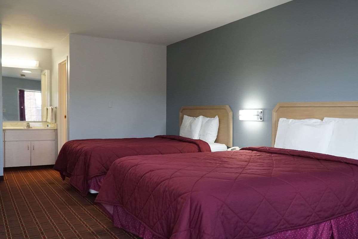 A hotel room with two beds, a bathroom, and a mirror.