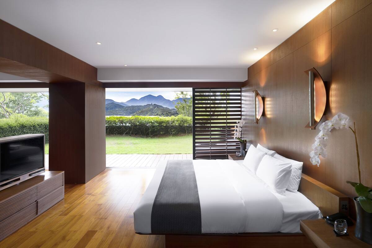 A modern bedroom with a large bed, a TV, and a view of a mountainous landscape.