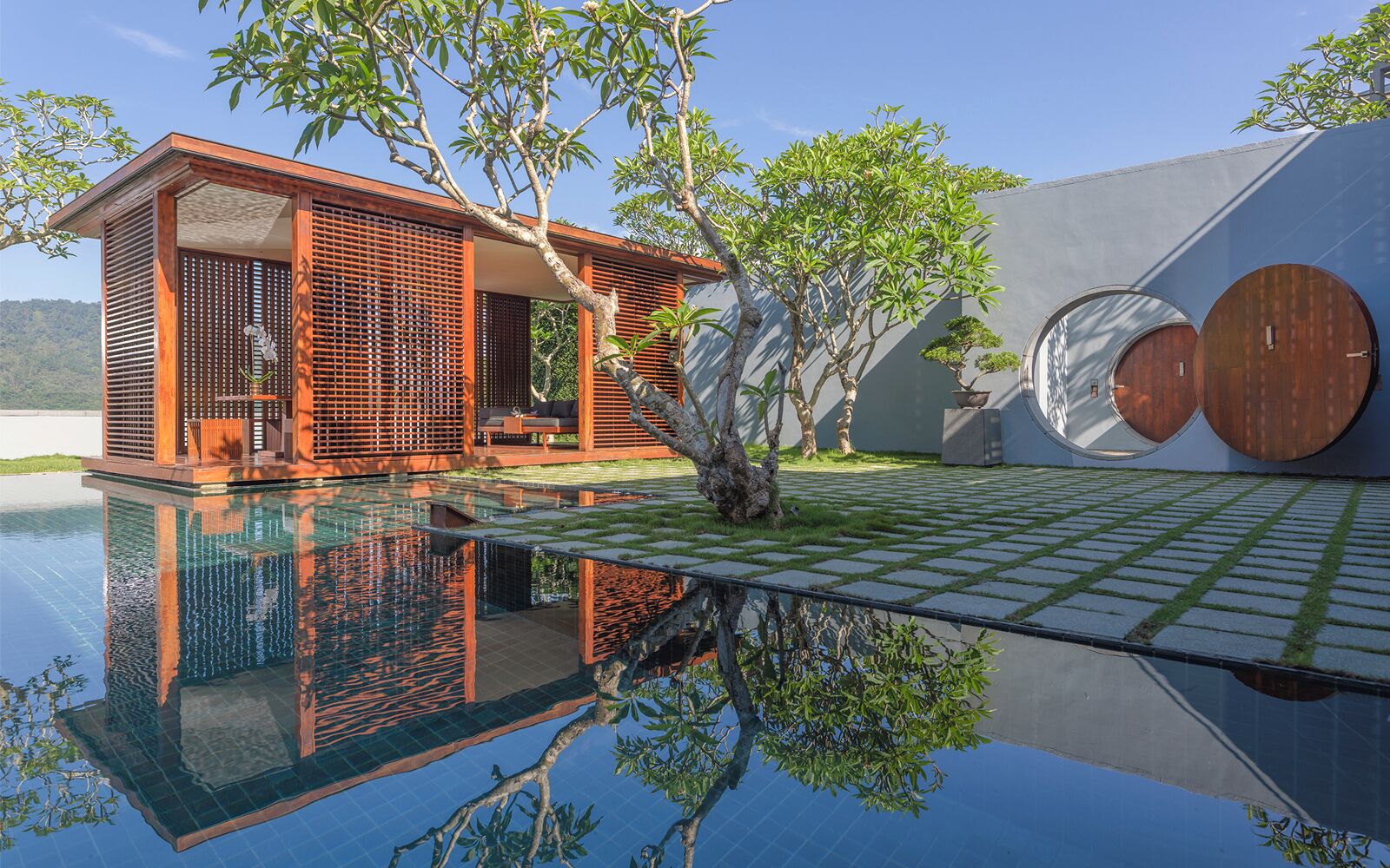 A modern building with a glass infinity pool, wooden deck, and a view of the water.