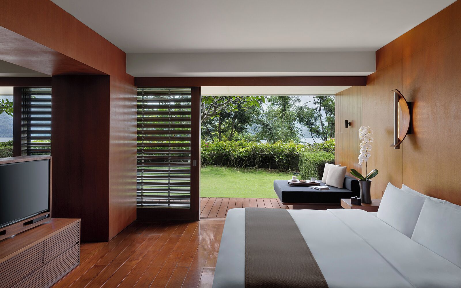 A modern hotel room with a large bed, a TV, a desk with a chair, and a view of the outdoors.