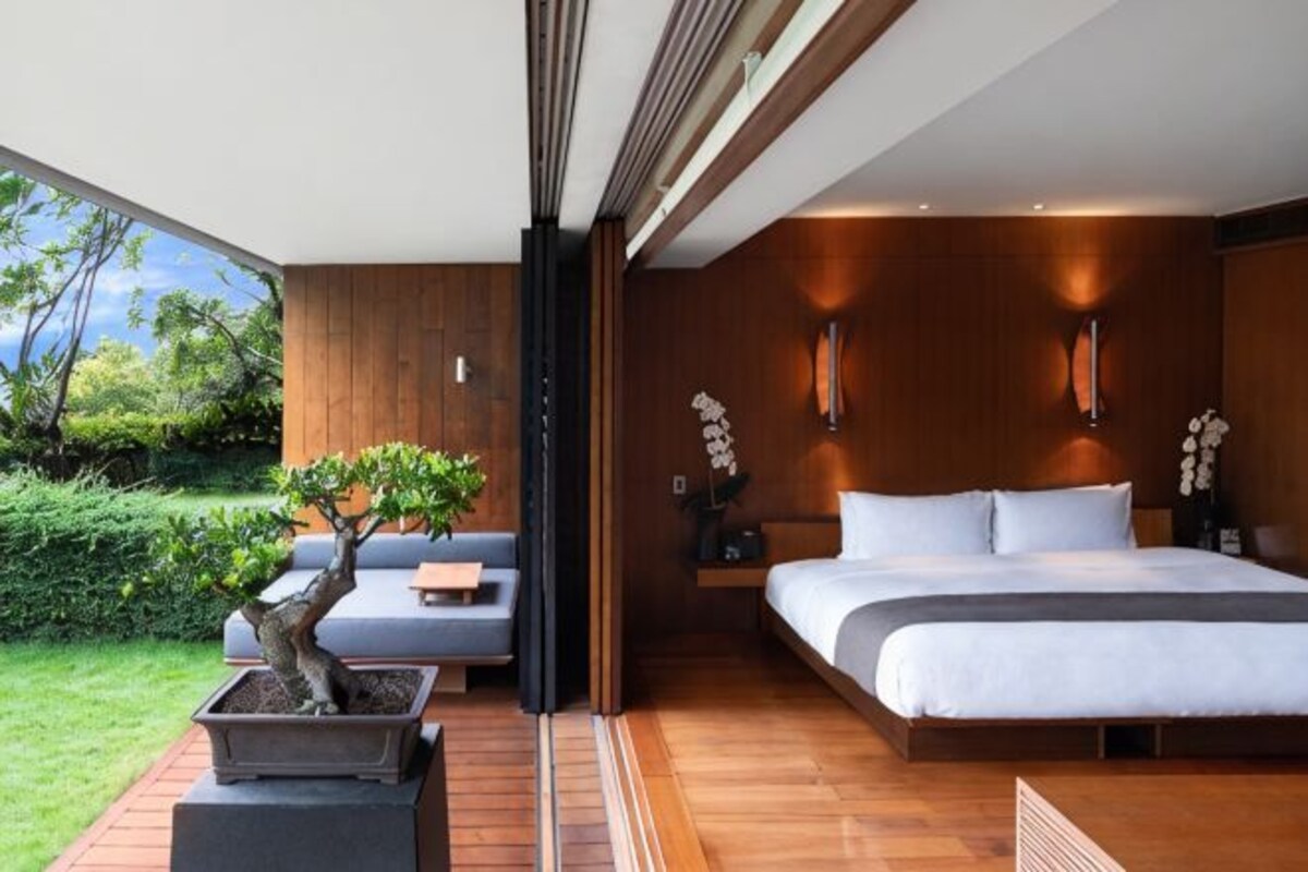 A modern bedroom with a large bed, a seating area, and a view of the outdoors.