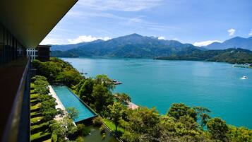 A view of a lake with mountains in the background, a pool, and a building with a balcony overlooking the scenery.