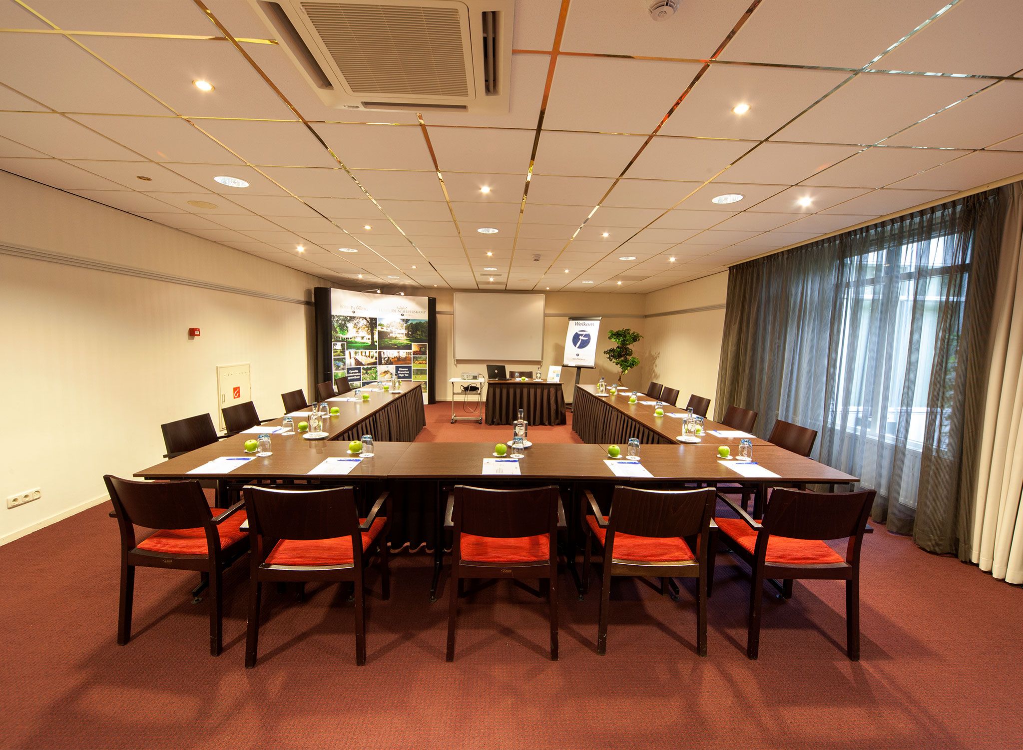 A conference room with a long table, chairs, a projector screen, and a banner.