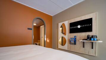 Habitación de hotel con una cama grande, televisión montada y una cafetera en un estante.