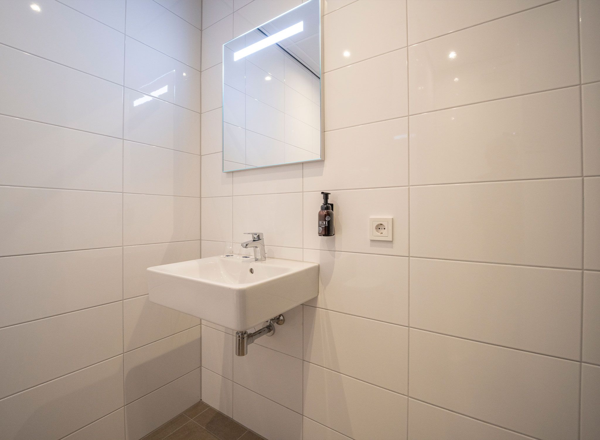 A bathroom with a white sink, a mirror, and a bottle of soap.