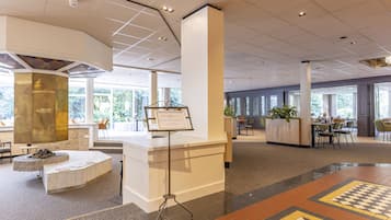 Eine geräumige Lobby mit einer Rezeption, Sitzbereichen und großen Fenstern mit Blick ins Freie.