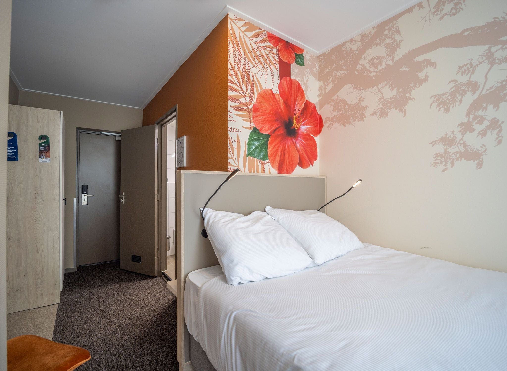 A hotel room with a bed, a door, and a wall with a floral mural.