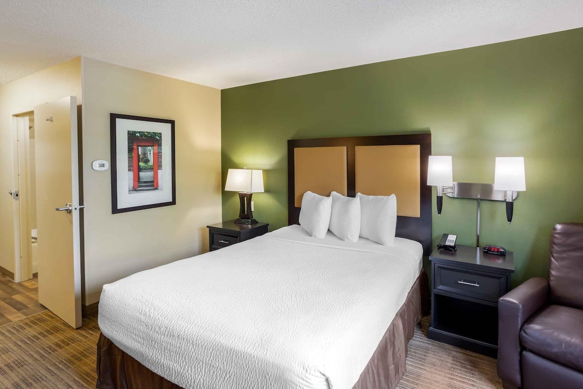 A hotel room with a large bed, two bedside tables with lamps, a chair, and a door leading to another room.