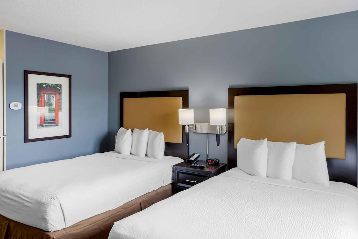 A hotel room with two beds, a nightstand with a lamp, and a framed picture on the wall.
