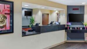 A reception area with a counter, a television, a fire alarm, and a framed artwork. - Extended Stay America Suites New York City LaGuardia Airport (Whitestone)