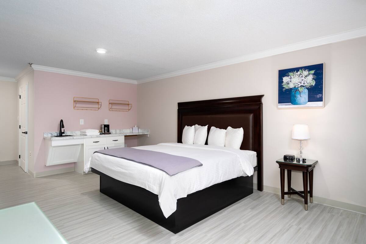 A hotel room with a bed, bedside table, lamp, and a painting on the wall.