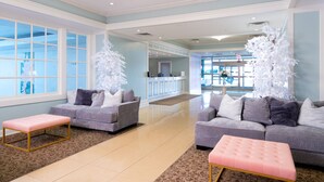 A spacious lobby with two grey sofas, a pink ottoman, and white artificial trees. - Bella Vista Hotel & Suites (Lynchburg)