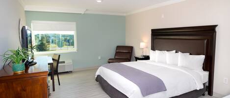 A hotel room with a large bed, a desk with a chair, a TV, and a window with a view of greenery.