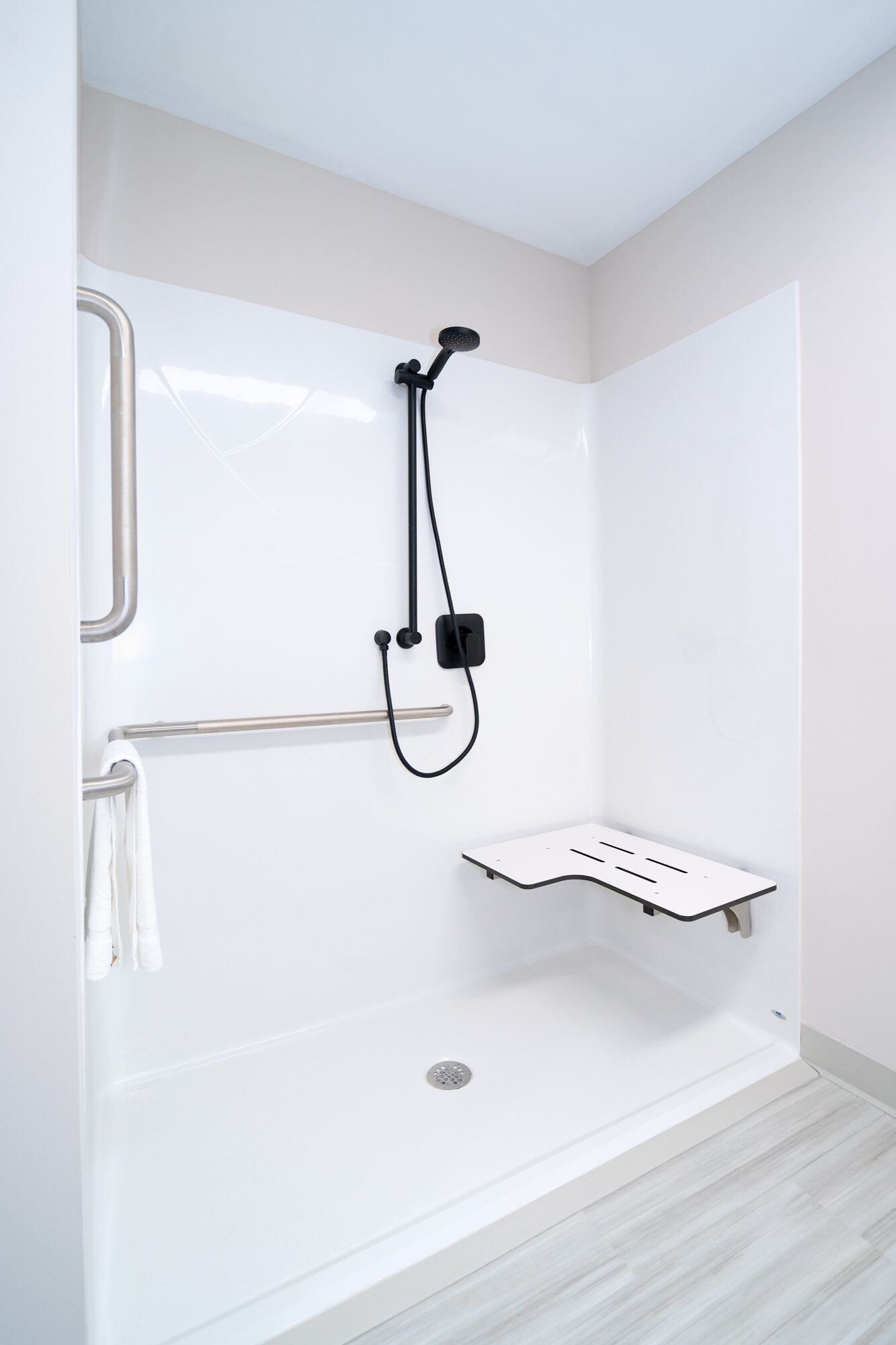 Un espace douche moderne équipé d’un pommeau de douche à main, d’un flexible de douche et d’une barre d’appui.