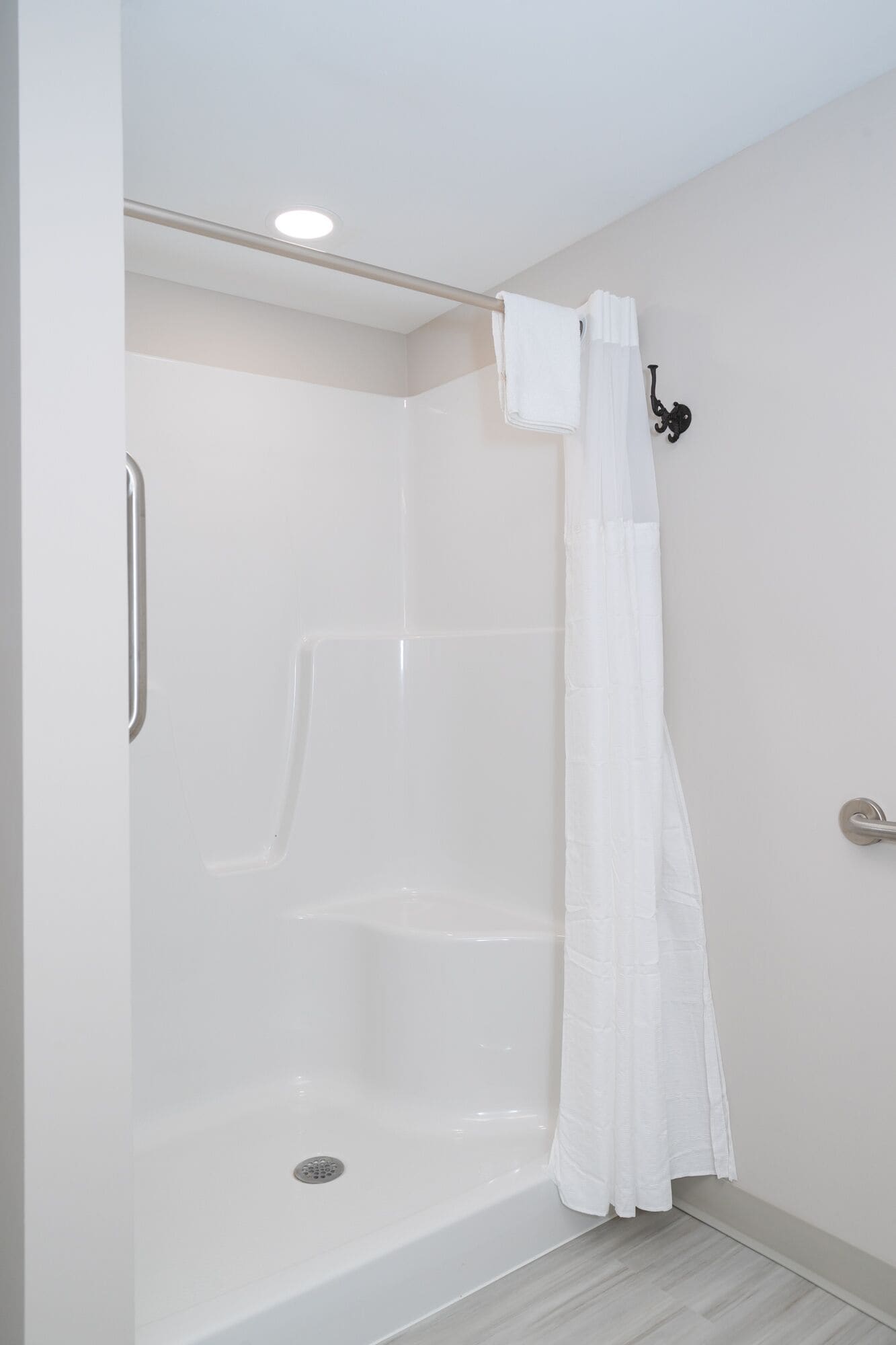Un box de ducha blanco con puerta de cristal, una barandilla de metal y una toalla blanca colgada en la pared.
