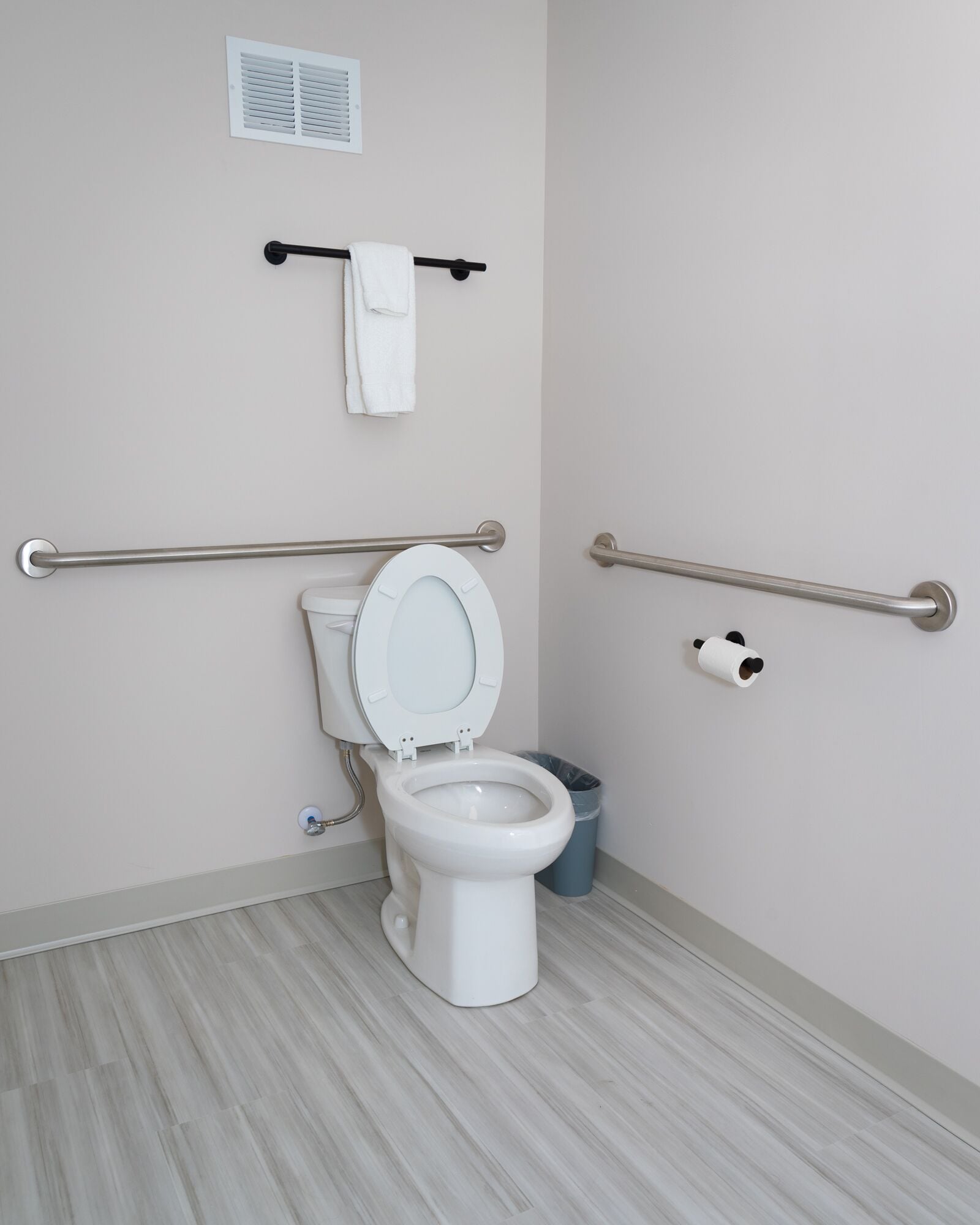 Un baño moderno con inodoro, barras de apoyo, toallero y cubo de basura.