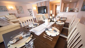 A dining room with a long table set for six, a sofa, and a TV in the background. - Bella Vista Hotel & Suites (Lynchburg)