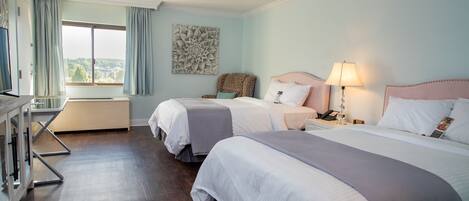 A hotel room with two beds, a desk, a chair, and a large window with curtains.