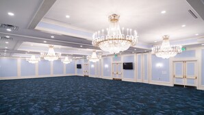 A large, well-lit room with multiple chandeliers, a flat-screen TV mounted on the wall, and a patterned carpet. - Bella Vista Hotel & Suites (Lynchburg)