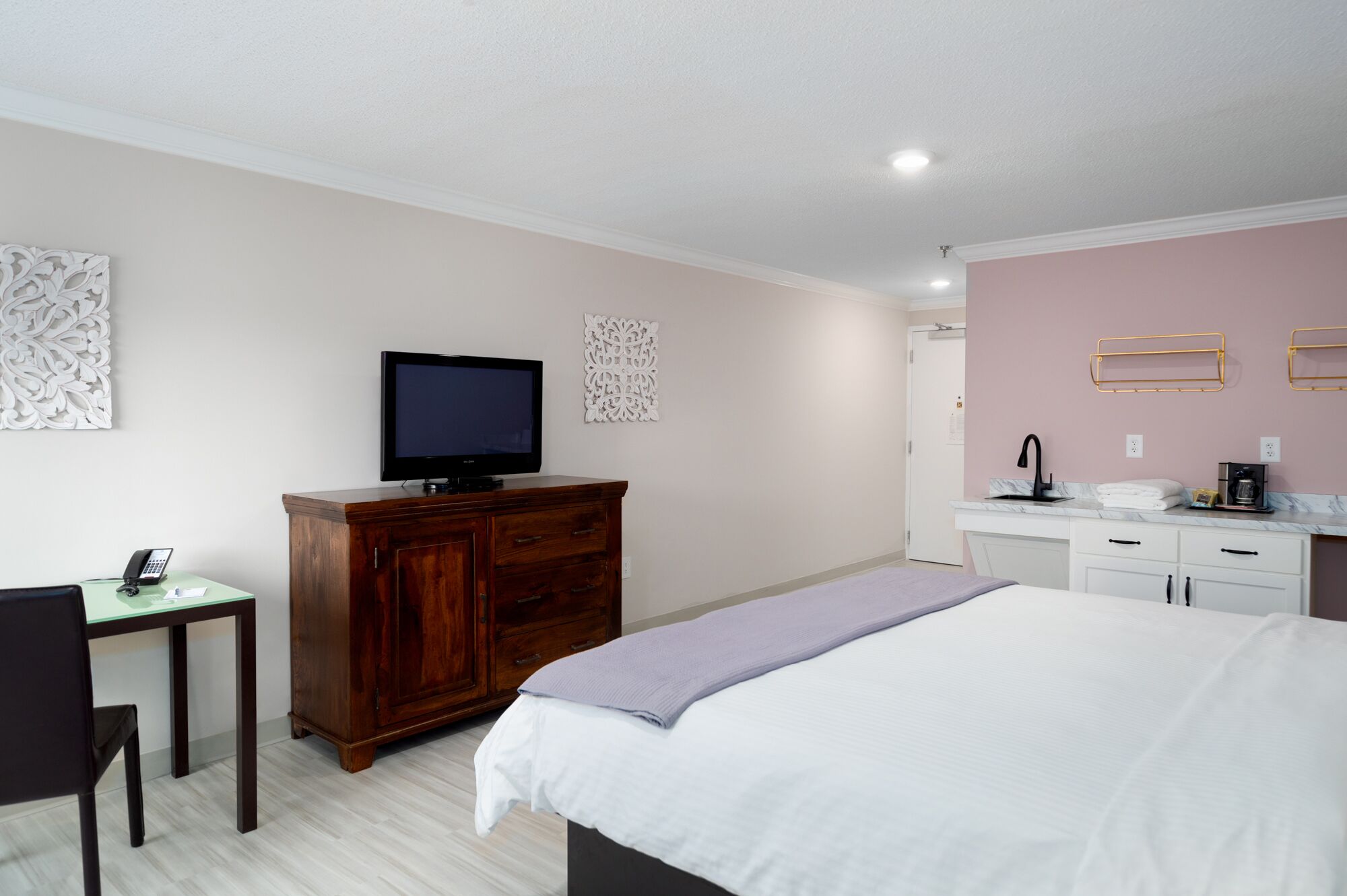 A hotel room with a bed, a desk with a telephone, a television, and a bathroom with a sink and mirror.