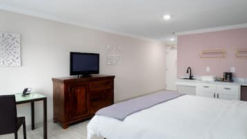 Hotelkamer met een bed, een bureau met telefoon, een televisie en een badkamer met wastafel en spiegel.