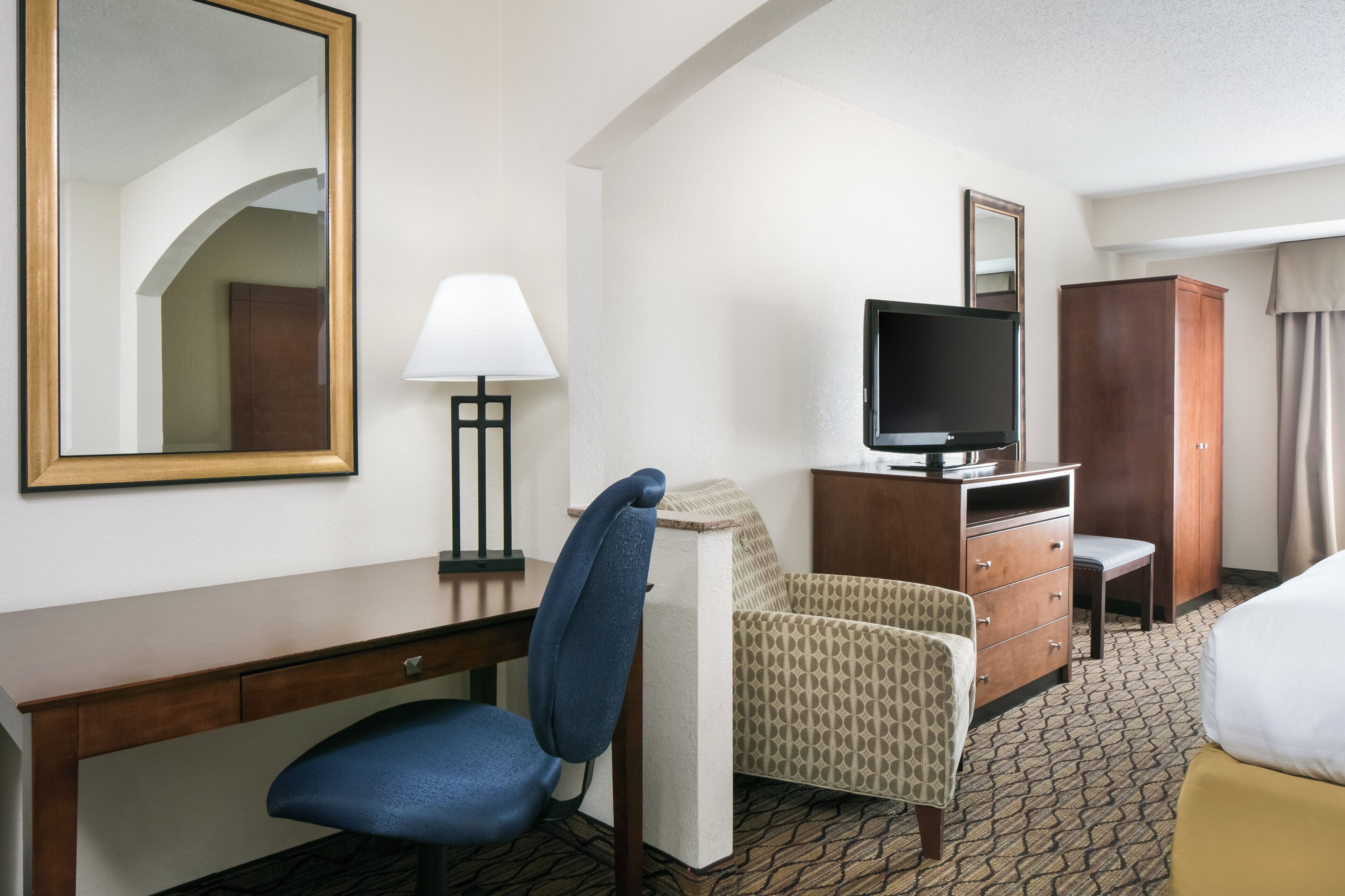 A hotel room with a desk, a chair, a television on a wooden cabinet, a wardrobe, and a bed.