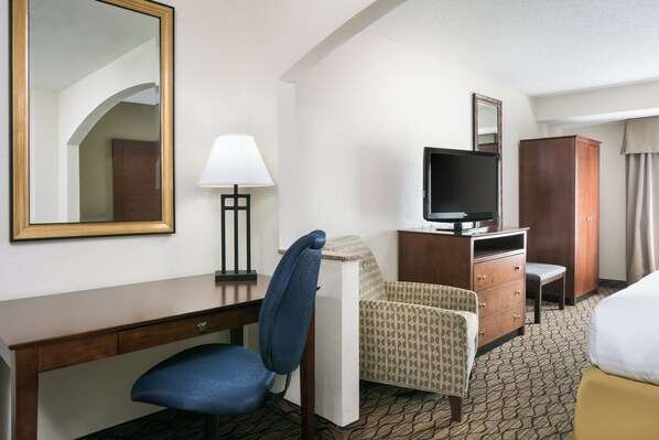 A hotel room with a desk, a chair, a television on a wooden cabinet, a wardrobe, and a bed.