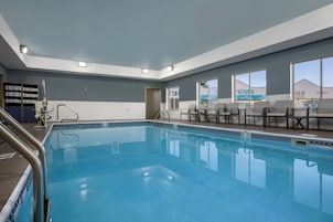 A swimming pool with a tiled edge, a metal ladder, and a door leading to another room.