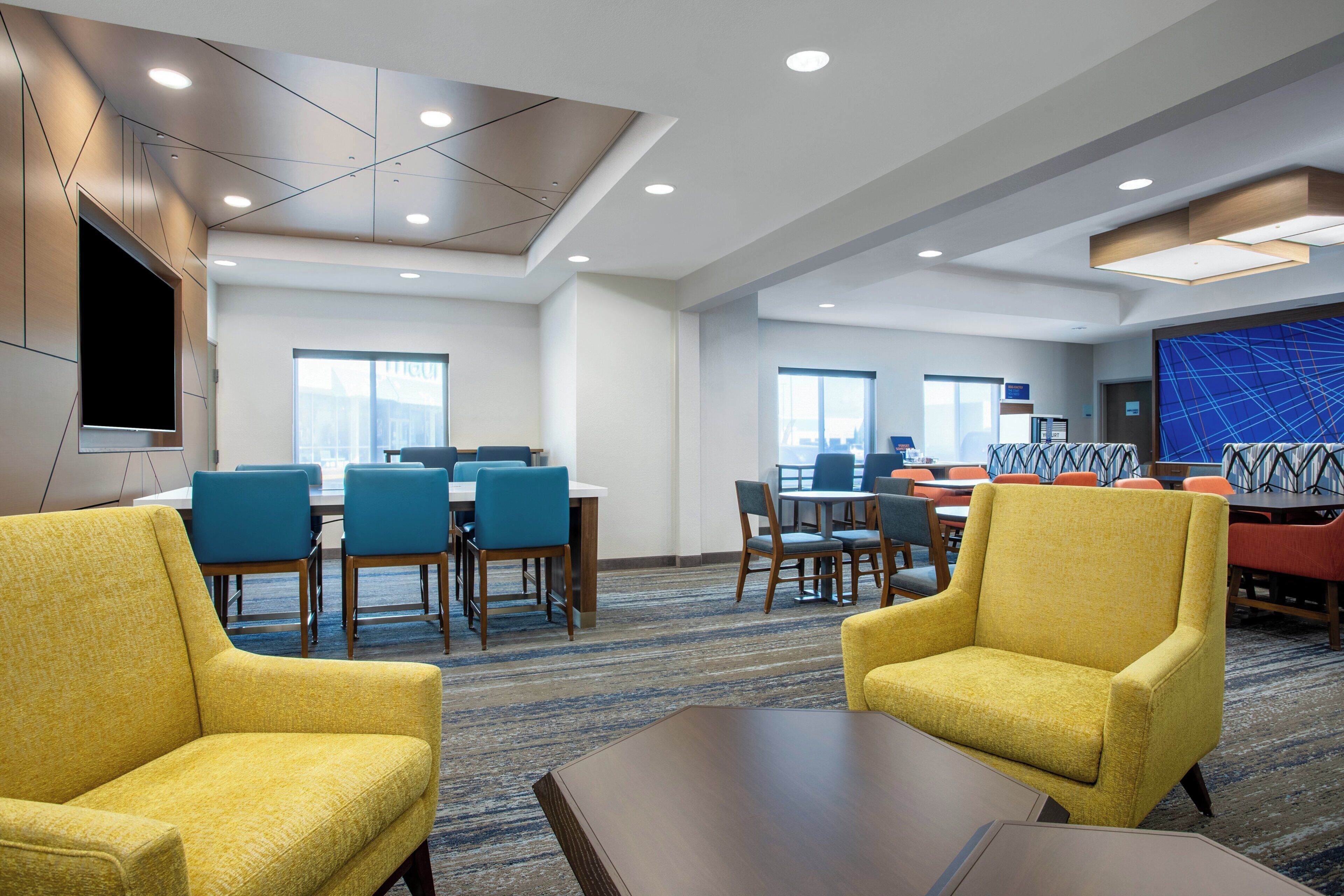 A hotel conference room with tables, chairs, and a large screen.