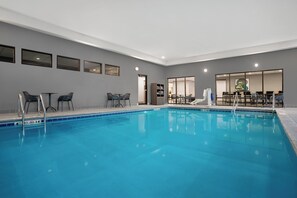 A swimming pool with lounge chairs and a table, surrounded by a neutral-toned room with framed artwork on the walls.