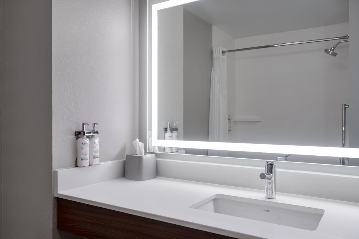 A modern bathroom with a large mirror, a white sink, and a shower area.