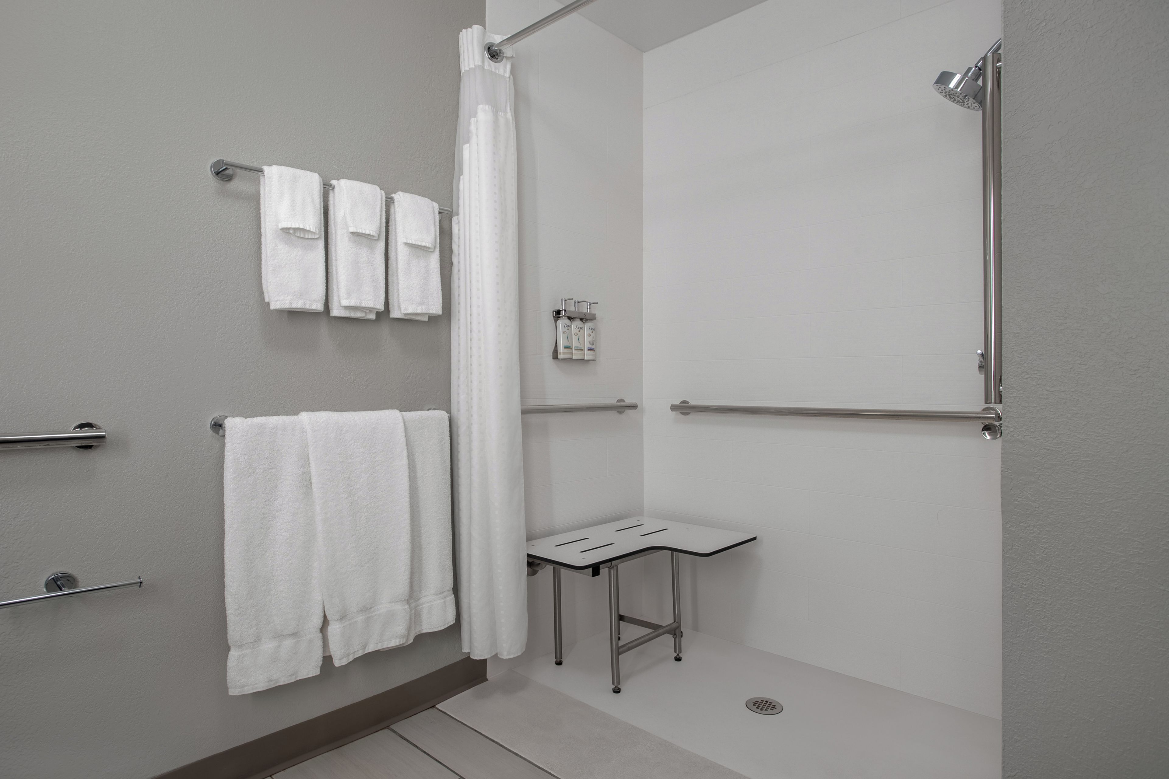 Un baño moderno con ducha, una mesita pequeña y varias toallas.