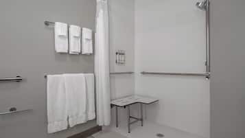 Un baño moderno con ducha, una mesita pequeña y varias toallas.