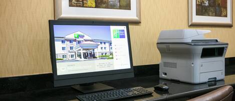 Una computadora de escritorio con un monitor que muestra un sitio web de hotel, un teclado e impresora sobre un escritorio.