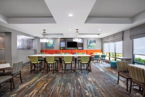 A modern hotel dining area with a large table, multiple chairs, and a colorful carpet. - Holiday Inn Express Hotel & Suites Clinton by IHG (Clinton)