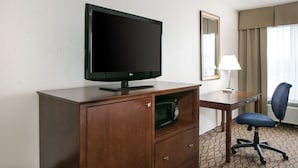A hotel room with a flat-screen TV on a wooden cabinet, a desk with a lamp, a chair, and a microwave. - Holiday Inn Express Hotel & Suites Clinton by IHG (Clinton)
