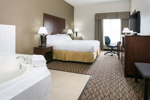 A hotel room with a large bed, two bedside tables with lamps, a desk with a chair, a TV, and a bathroom with a sink and mirror.