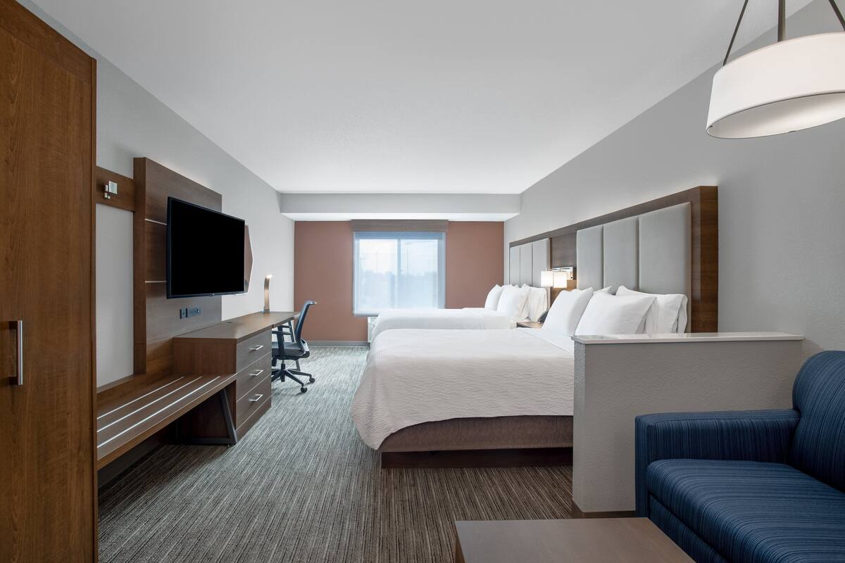 A hotel room with a large bed, a desk with a flat-screen TV, a blue sofa, and a large window with a view.