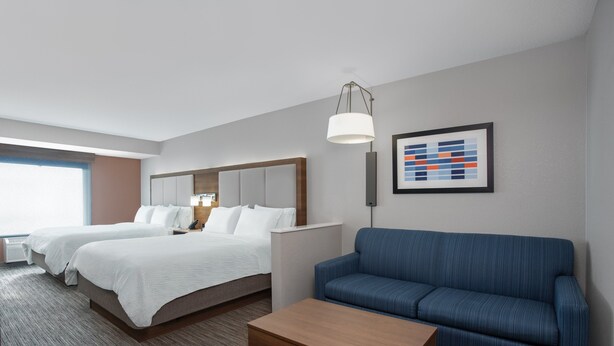 A hotel room with two beds, a blue sofa, a wooden coffee table, and a framed abstract art piece on the wall.