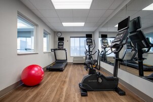 A gym with treadmills, an elliptical, a red exercise ball, and a clock on the wall.