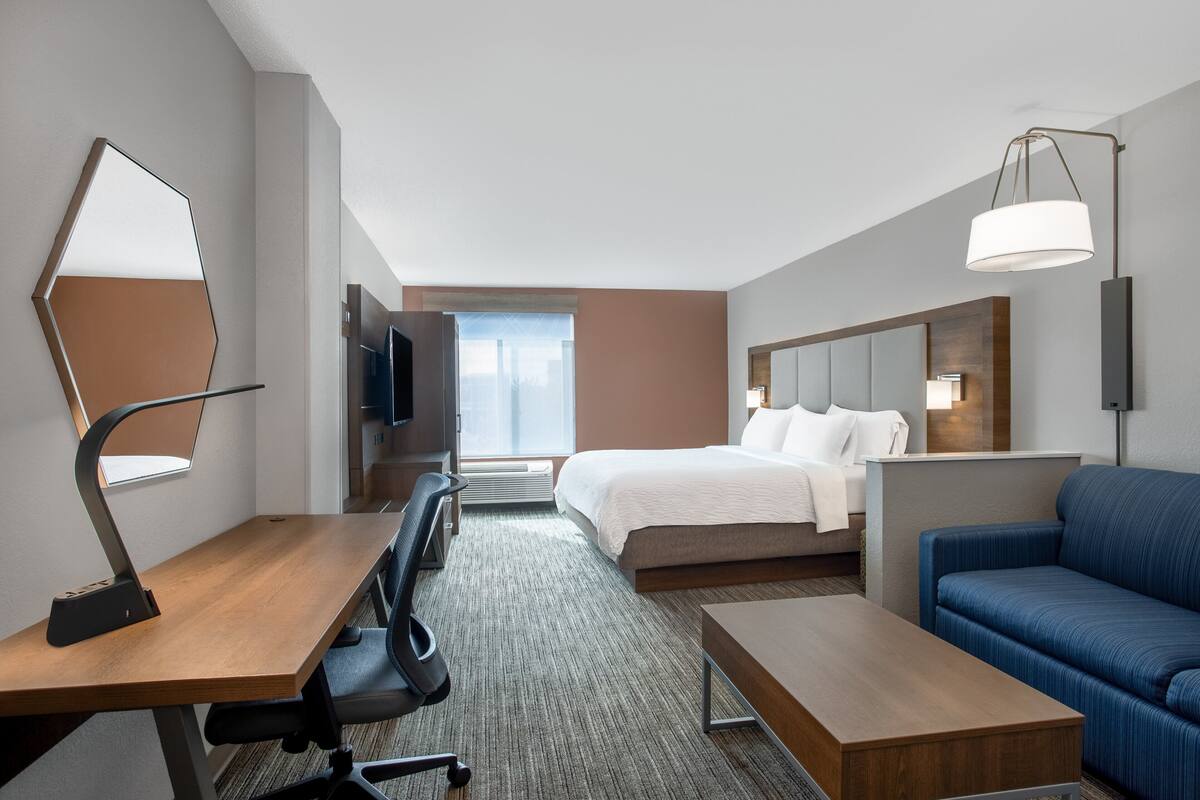 A hotel room with a bed, a desk with a lamp, a sofa, and a TV.